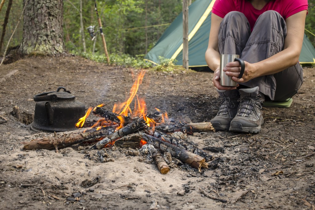 Girl Sitting While Camping Near The Fire Heated And Drink Hot Te
