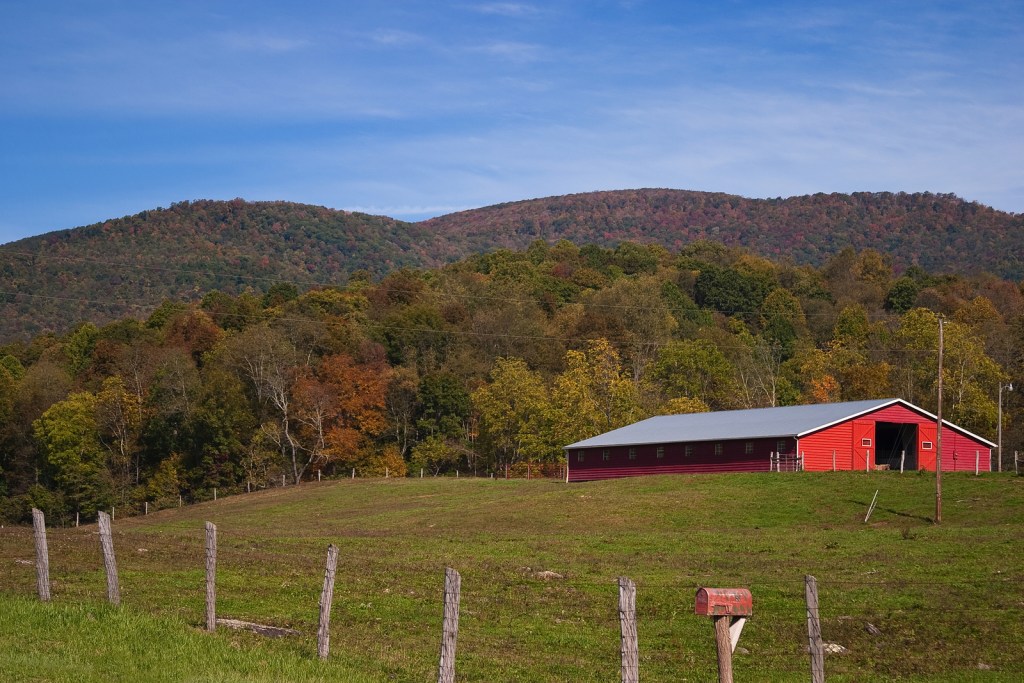 A modern red barn in the hills during autumn.