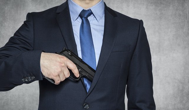 businessman with a gun, grey background with copy space