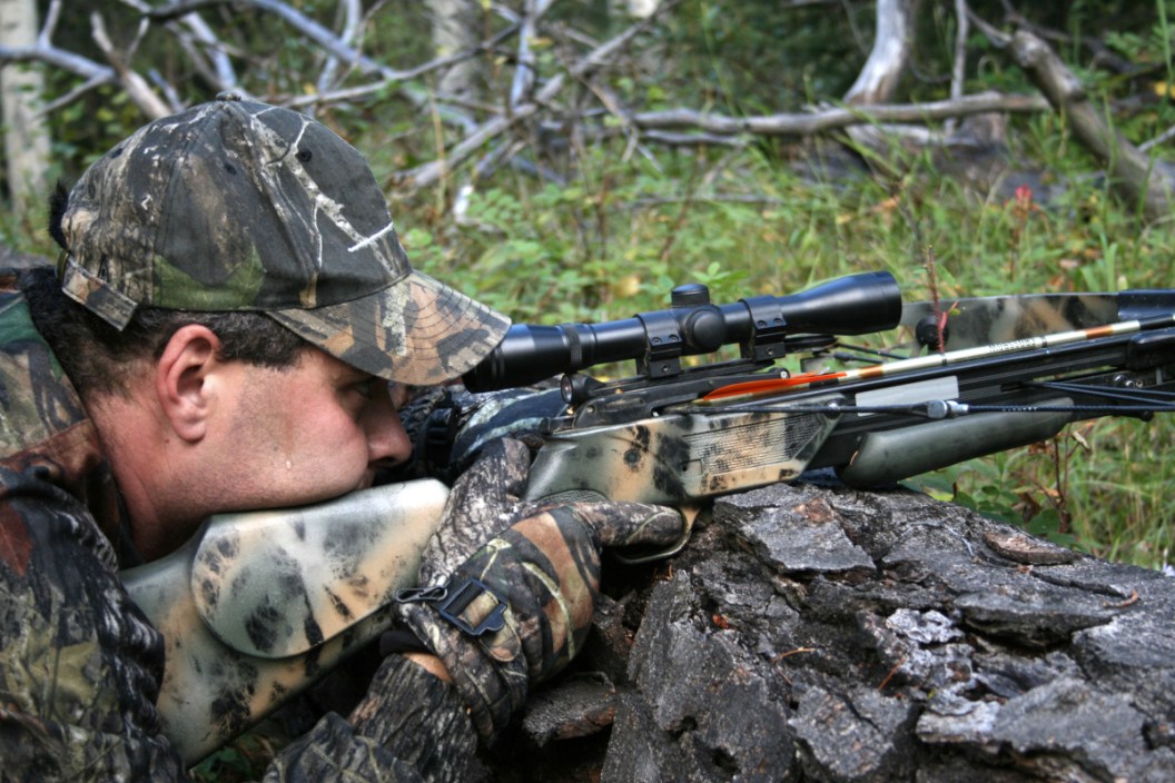A hunter aiming a crossbow in the woods.
