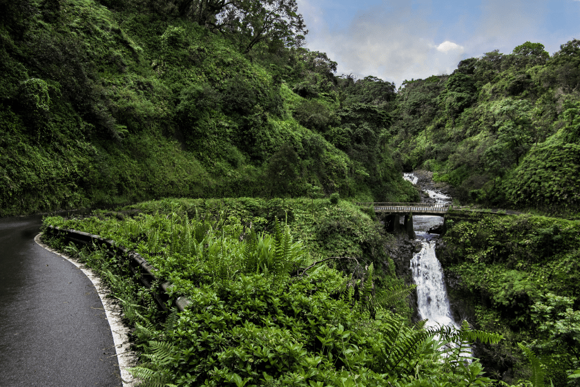 The Hana Highway turns to cross a one lane bridge beside a waterfall on the north coast of Maui.