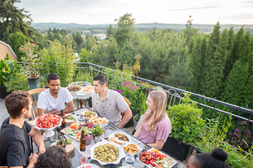 A multiethnic group of young friends enjoy good food and conversation together on a terrace outside on a summer evening. The shot is from overhead.