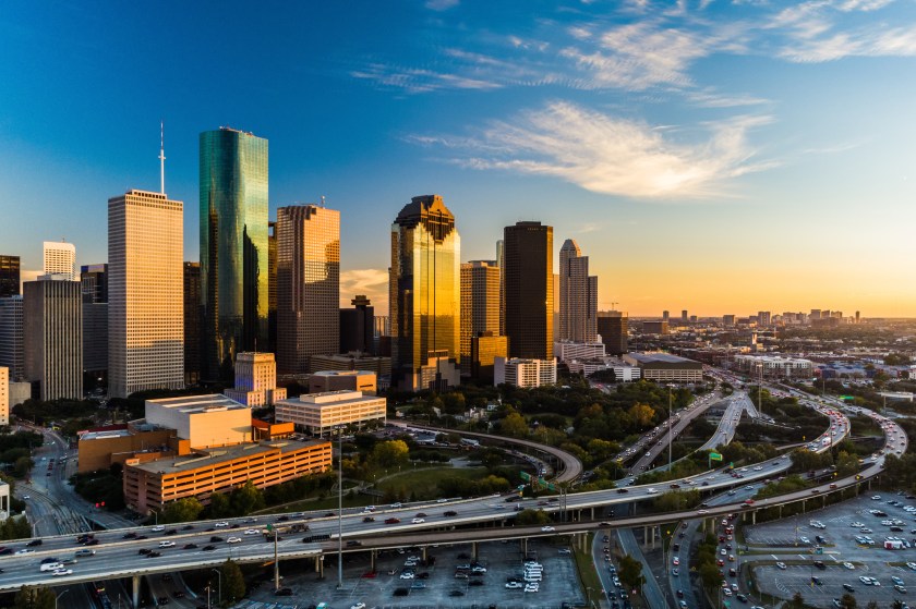 Downtown Houston skyline aerial at sunset with a highway in the foreground, angled view with the Texas Medical Center in the far distance