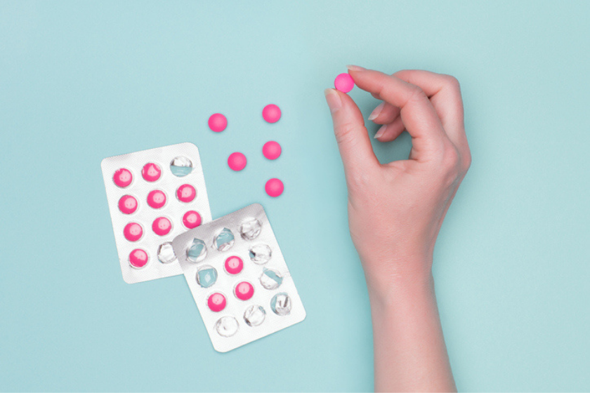 Woman's hand holding pink tablets, resembling Benadryl.