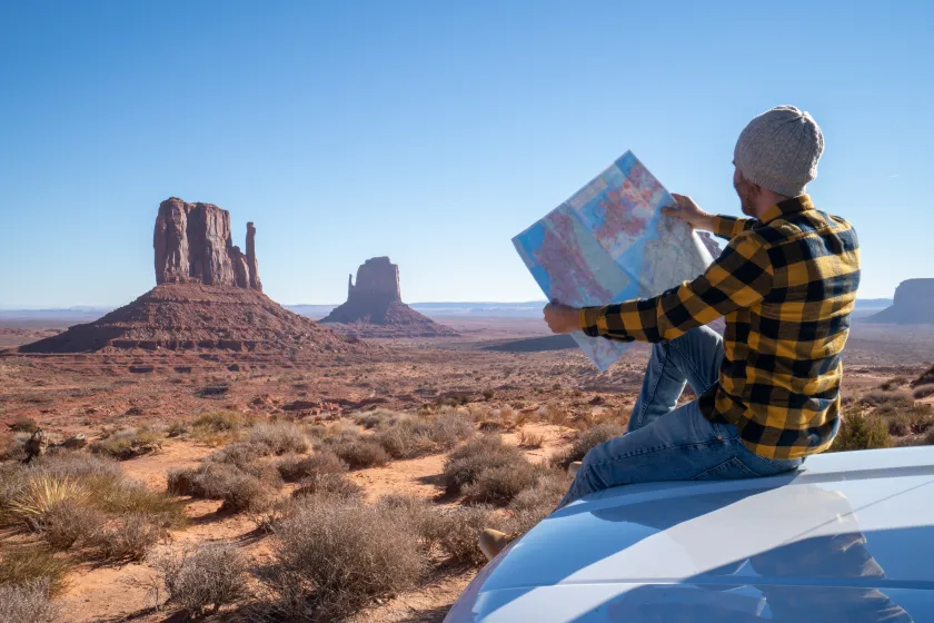 Young man outside car looking at road map for directions exploring national parks and nature ready for adventure