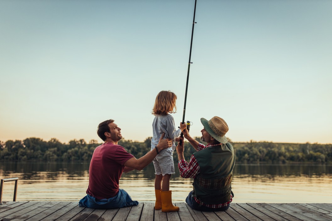 Grandfather, father and little boy are fishing at the river