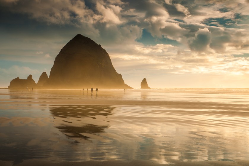 Oregon's Cannon Beach at sunset and in between storms. People can be seen strolling on the beach.