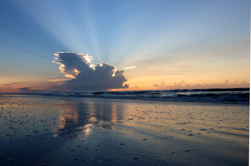 Marine landscape with sunbeams from sun rising from the cloud and beautiful reflection in a shallow ocean water. Huntington Beach State Park, Litchfield, Myrtle Beach area, South Carolina