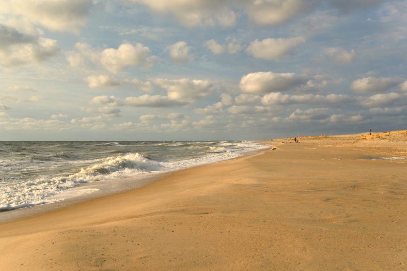 A lone individual walks the beach of Maryland's Assateague State Park on an Autumn morning with background of fluffy or puffy cumulus clouds overhead