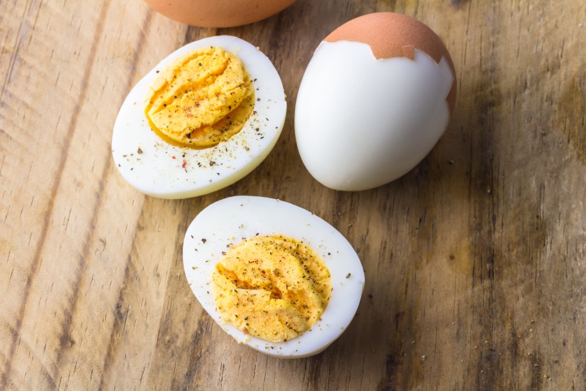 Hard-boiled eggs on wooden board with pepper flecks.
