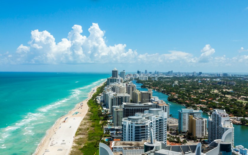 Looking down South Beach in Miami. Full view of the beach on the left and the city on the right. Beautiful blue sky on a clear day.