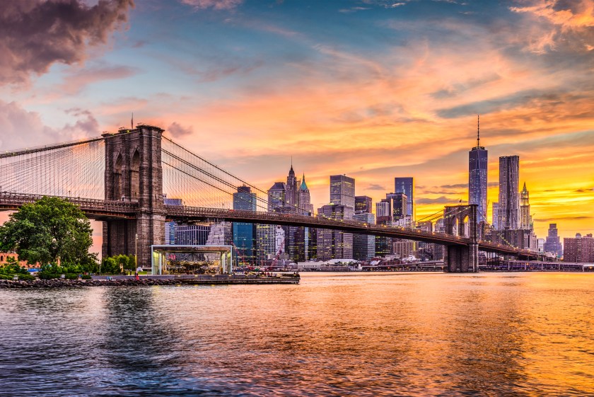 New York City Skyline on the East River with Brooklyn Bridge at sunset.