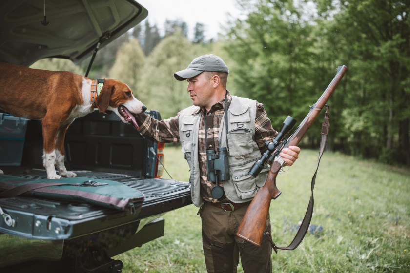 A shot of a hunter with riffle and his dog preparing for a hunt.