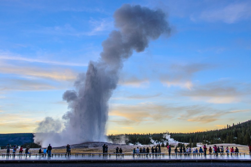 Groups of people have been waiting to watch, experience and photograph this Old Faithful eruption just after sunset on a sunny early autumn day.
