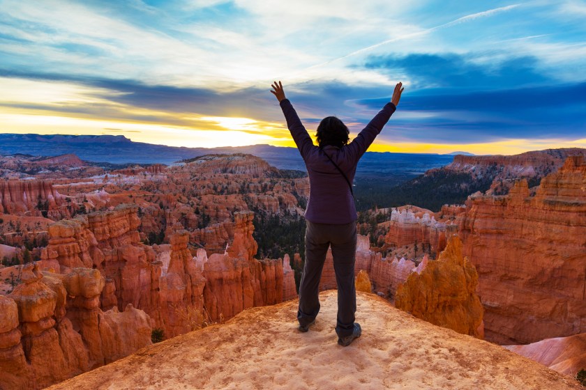 woman celebrates On top of Bryce Canyon with hands raised