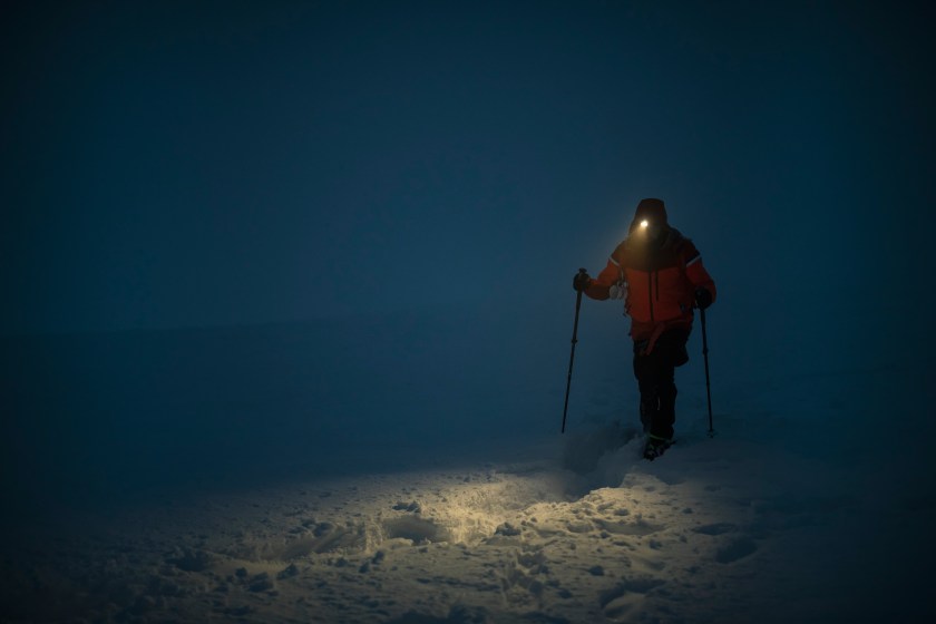 Cross country skiier wearing a headlight on a dark snowy trail.