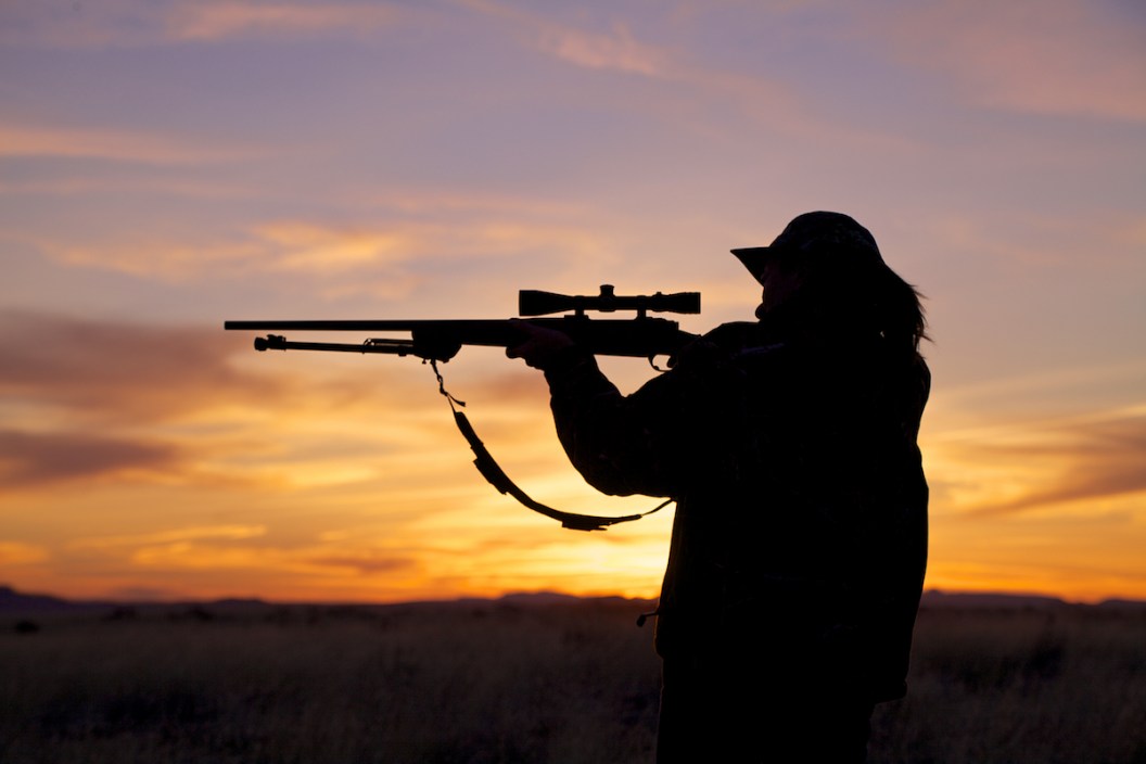 a woman hunter shooting her rifle silhouetted at sunset