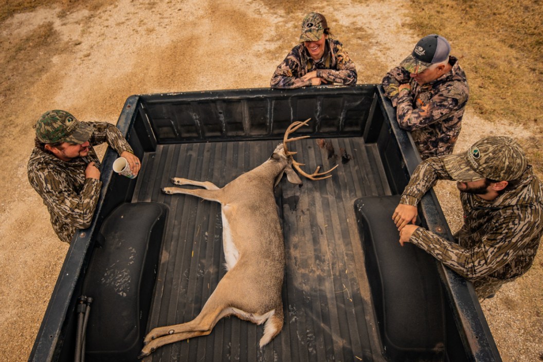 Hunters standing around a pickup with a freshly harvested deer.
