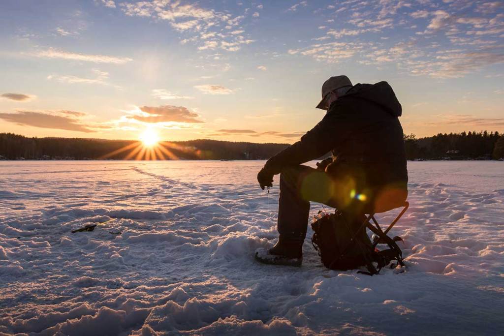 Ice fisherman sits on frozen lake