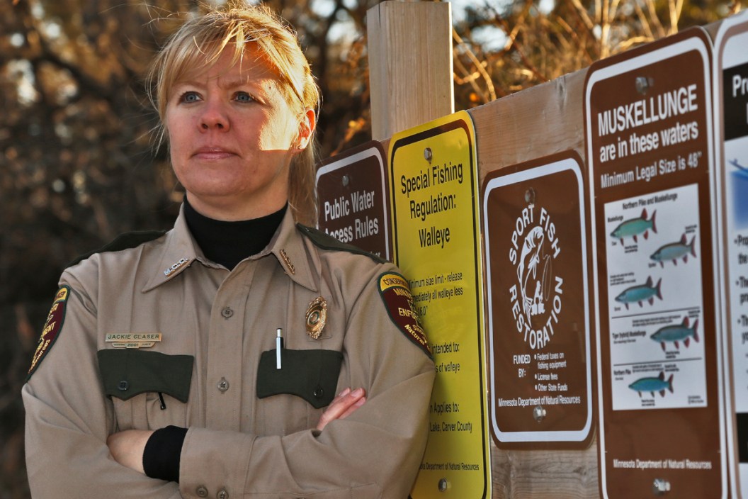 Minnesota Department of Natural Resources officer standing by a sign.