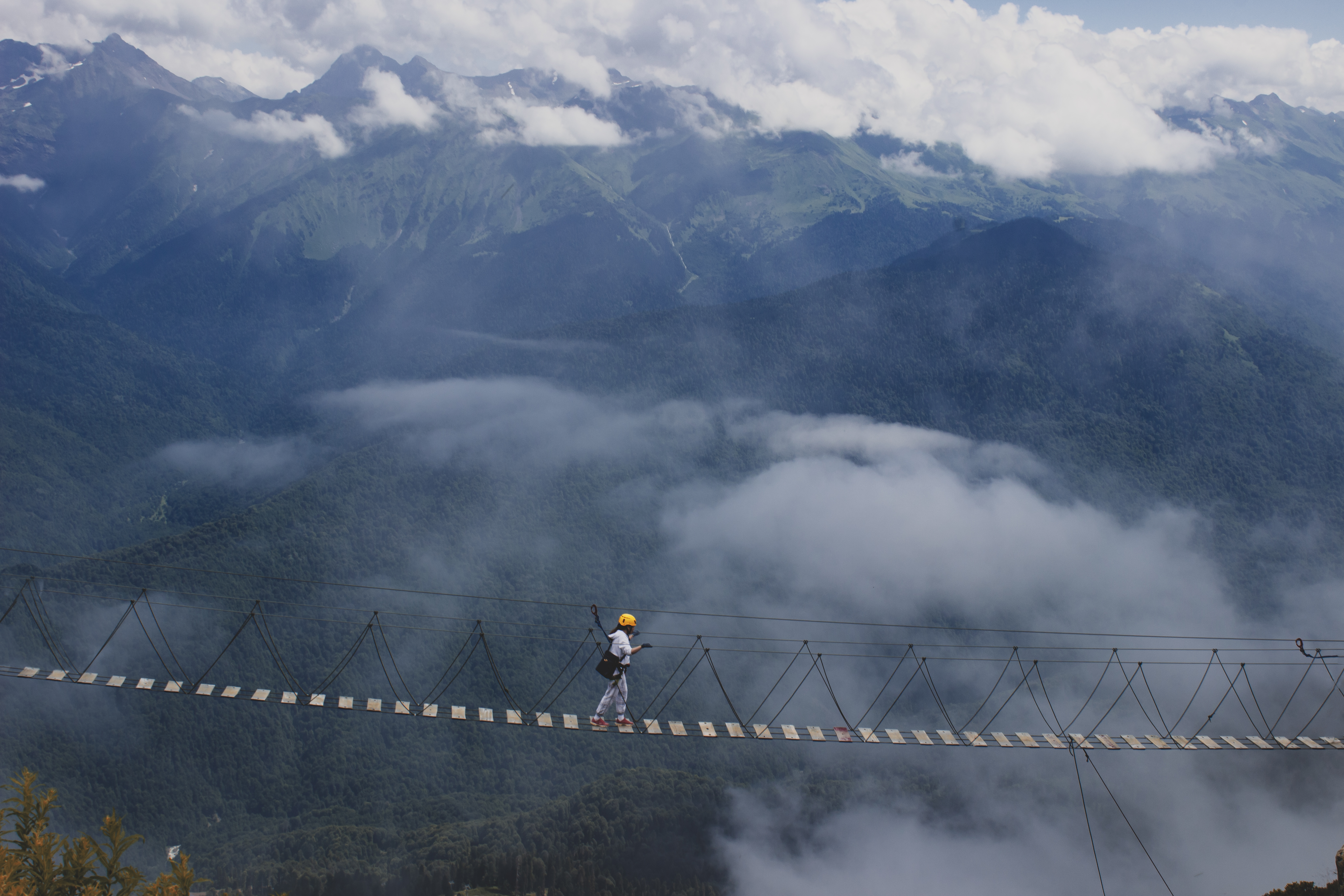 people walk on the suspension bridge over the cliff in 2000 m. next to them, light clouds,which give the picture even more focusцель