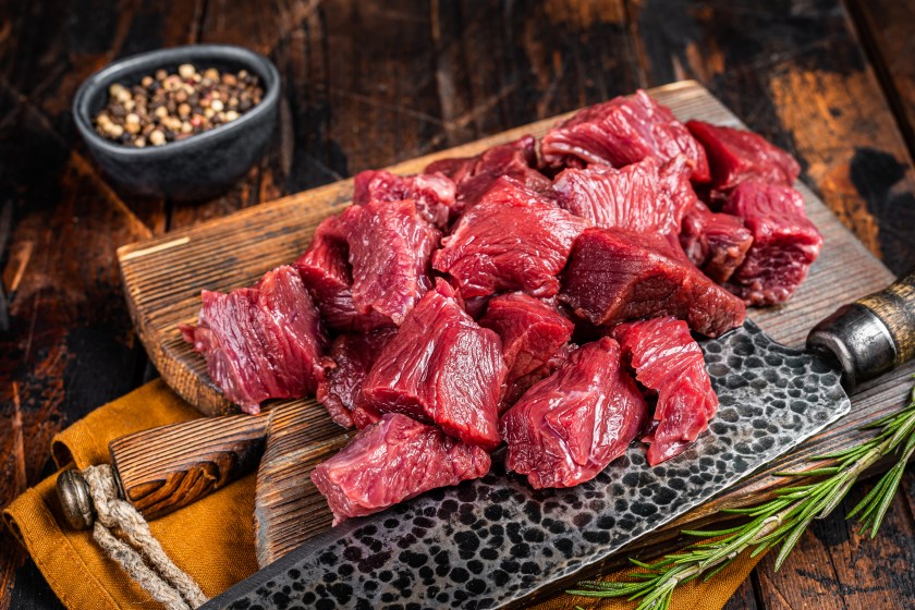 Sliced Raw venison dear meat for a stew, game meat on butcher cutting board. Wooden background. Top view.