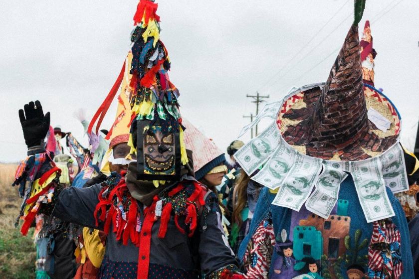 two revelers in colorful costumes and hats dance in a field