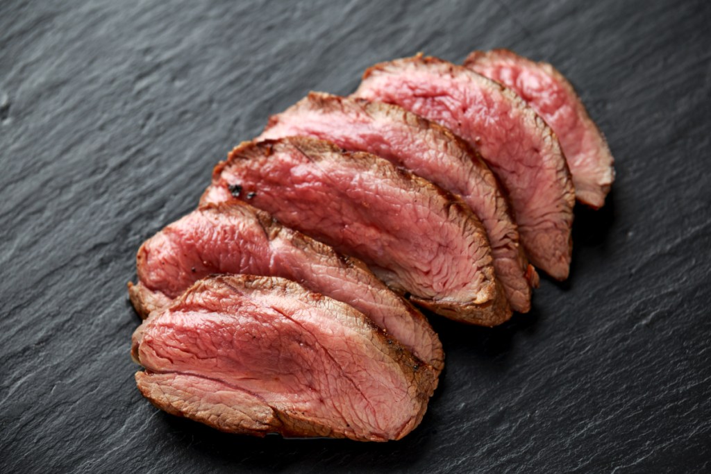 Slices of venison steak on a black table.