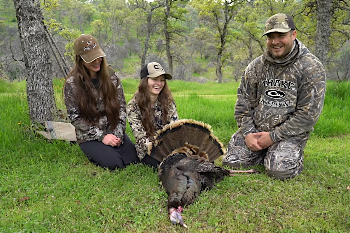 Hunters sitting around a harvested wild turkey.