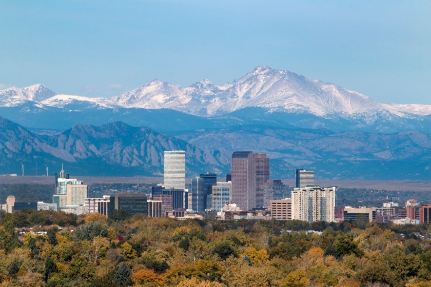 With the snow covered Longs Peak part of the Rocky Mountains and the iconic flatirons of Boulder in the background, Downtown Denver skyscrapers including the iconic "mailbox" or "cash register" building as well as hotels, office buildings and apartment buildings fill the skyline.