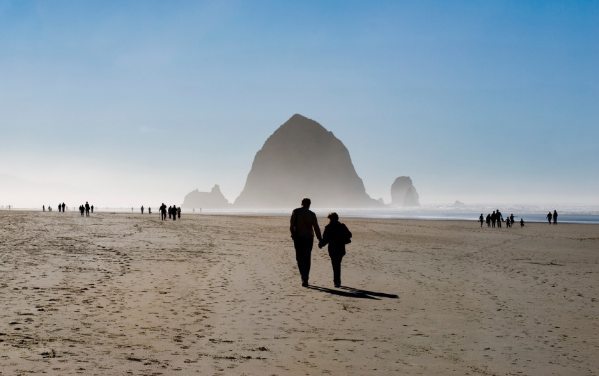 A couple walks hand in hand towards haystack rock on Cannon Beach, OR.
