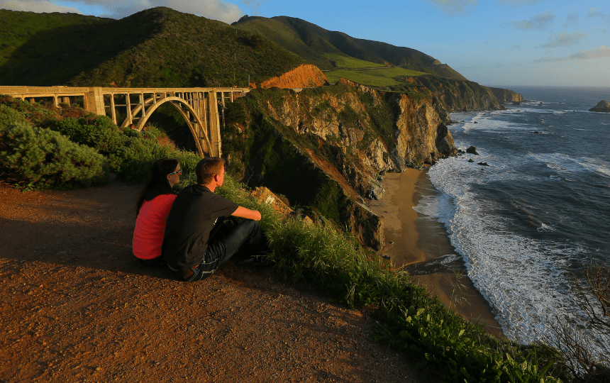 A couple enjoys a pacific sunset view from bixby creek bridge on the california coast.