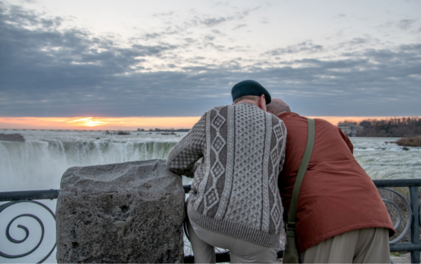Married Caucasian men in their late 60's still in love and playful at Niagara Falls, Ontario, Canada. The couple is touring the Falls at sunrise.