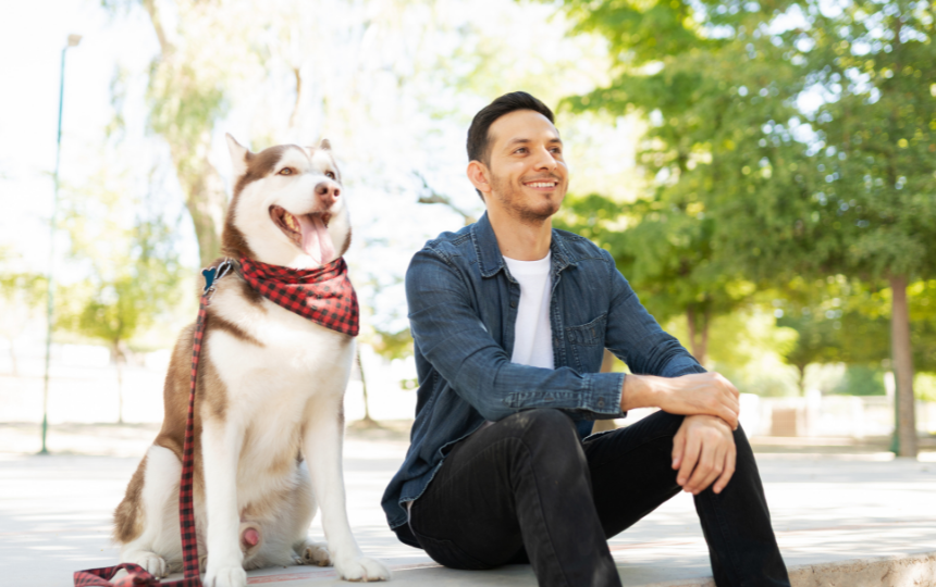 man sits with husky in park