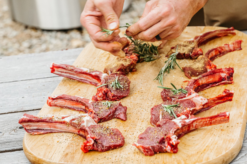 A hunter preparing wild game meat outside by the fire.