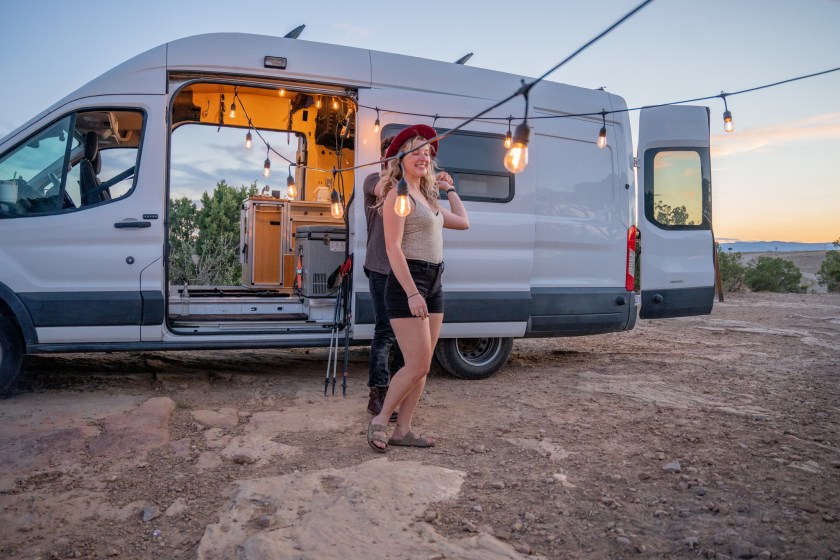 Girl near van under Edison bulbs in the desert