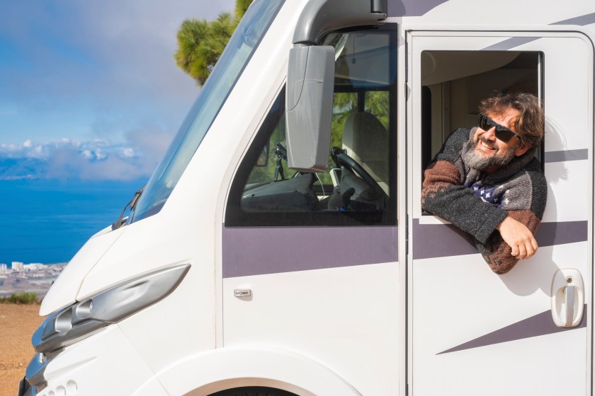 Cheerful happy tourist man smile and admire outside the driver windows of his modern white camper car motorhome