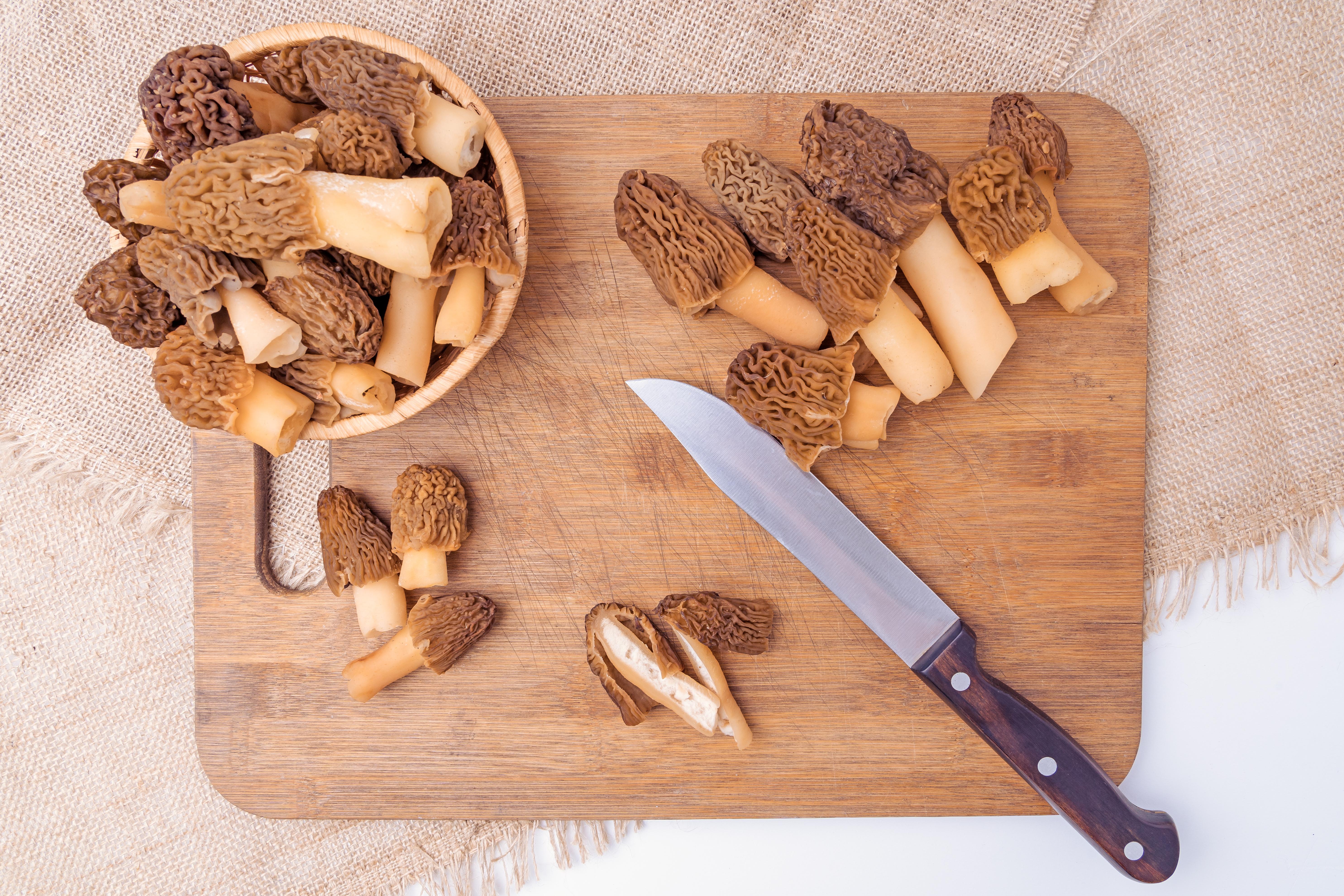 Raw morel mushrooms in a basket on a cutting board, top view