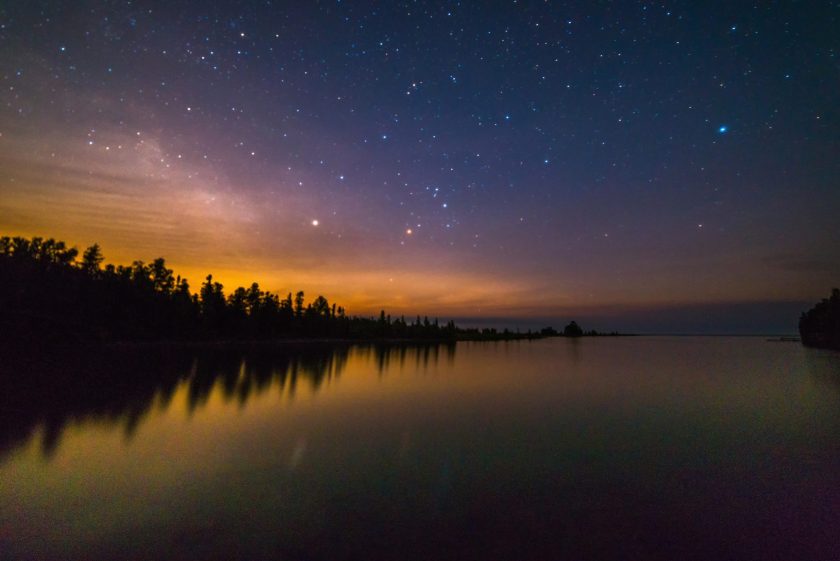 Lake Huron water reflecting with stars, trees and milky way at night near Tobermory, Bruce Peninsula, Ontario