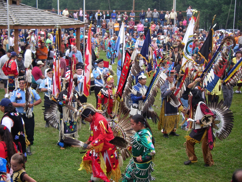 a large group of Chippewa dance in cultural garb