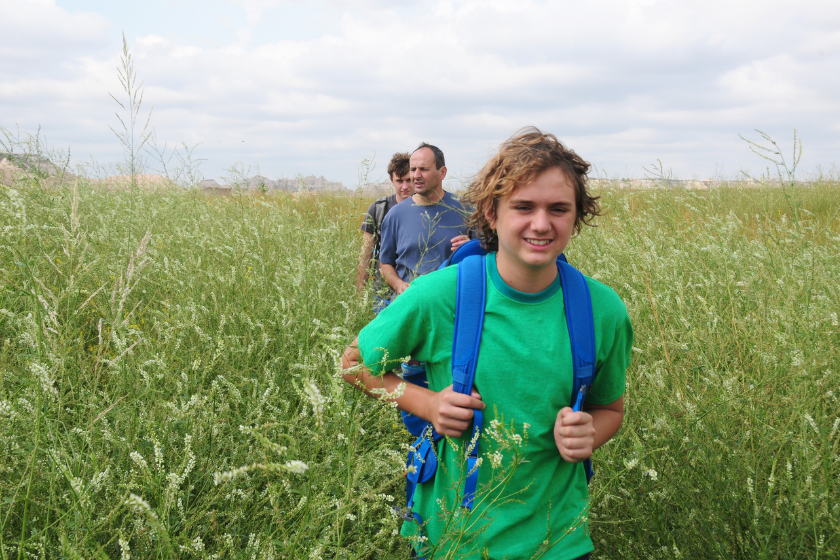 Father and teenager boys hiking in green field.