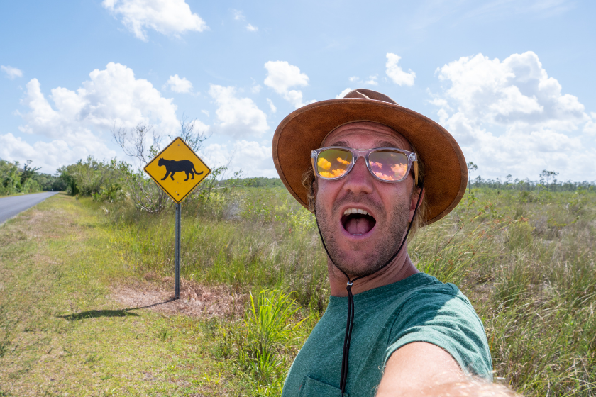 Young man taking selfie on empty highway road near Florida Panther warning sign