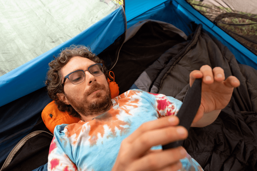 While tent camping a caucasian man in his 30s is wearing a tie dye t-shirt and spends time relaxing watching something on his mobile phone on a summer day in Hot Springs National Park Arkansas, USA.