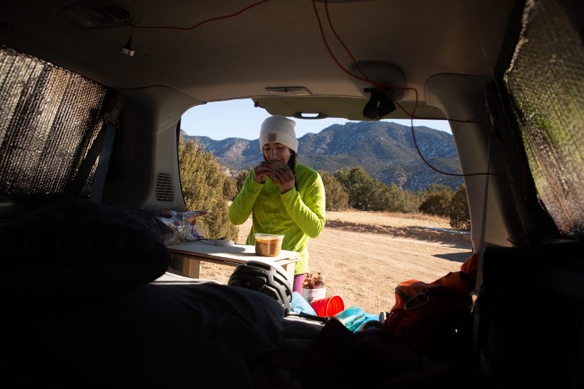 A woman makes breakfast out the back of her built out van where she stays during climbing trips