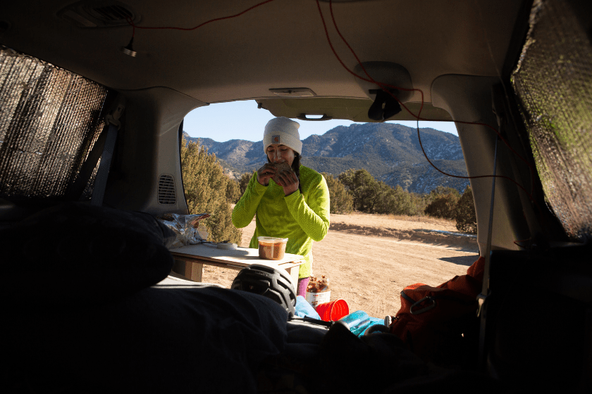 A woman makes breakfast out the back of her built out van where she stays during climbing trips