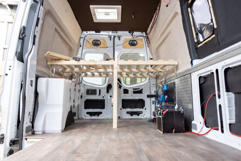 Interior view of a van being converted into a caravan. A wooden bed frame and other components already installed.