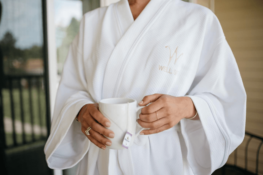 torso picture of a woman wearing a Wells Spa branded bathrobe holding a cup of tea