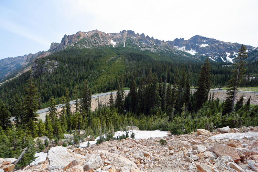 Rugged snow-capped peaks contrast with green evergreen trees along Highway 20 through the North Cascades in Washington State.