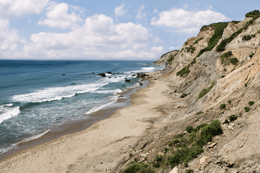 Ocean waves break on a sandy beach beneath the tall cliffs of Block Island, RI.