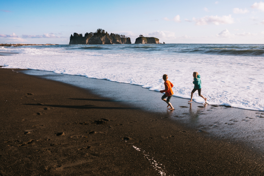 Beautiful textures and beach views of the Pacific Ocean from Washington States Olympic Peninsula. A boy and girl run from the splashing waves at the waters edge, the sunset casting pink and orange colors on the water.